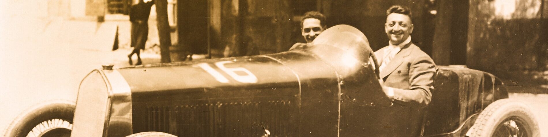 Black and white photo of Enzo Ferrari sitting in one of the first Ferrari cars