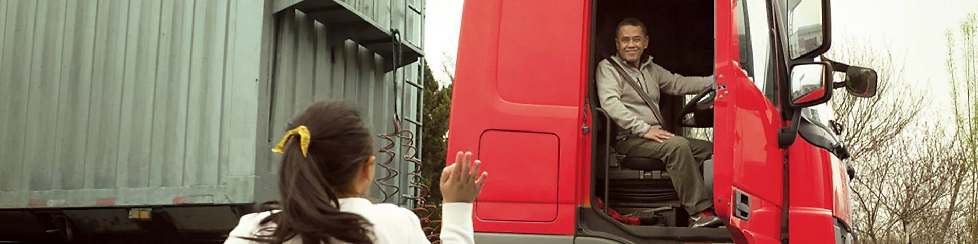 Man in red truck cab with door open waving to his daughter